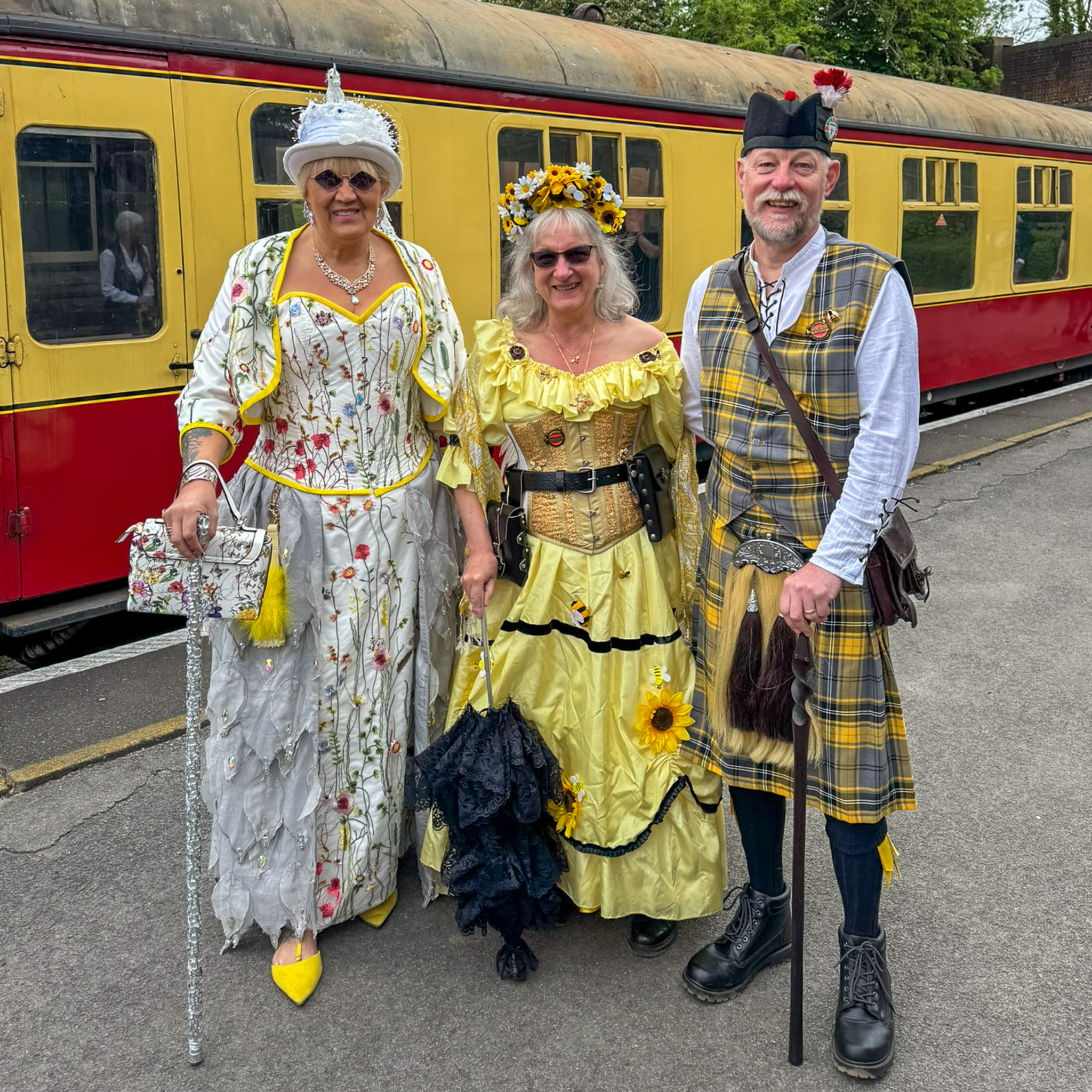 Three people in vintage costumes posing beside a yellow train car.
