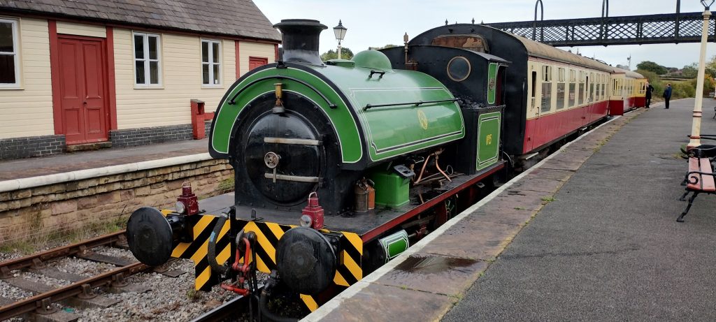 No15 - Midland Railway - Butterley Green steam locomotive on a platform with cream and red passenger carriages attached at a small railway station.