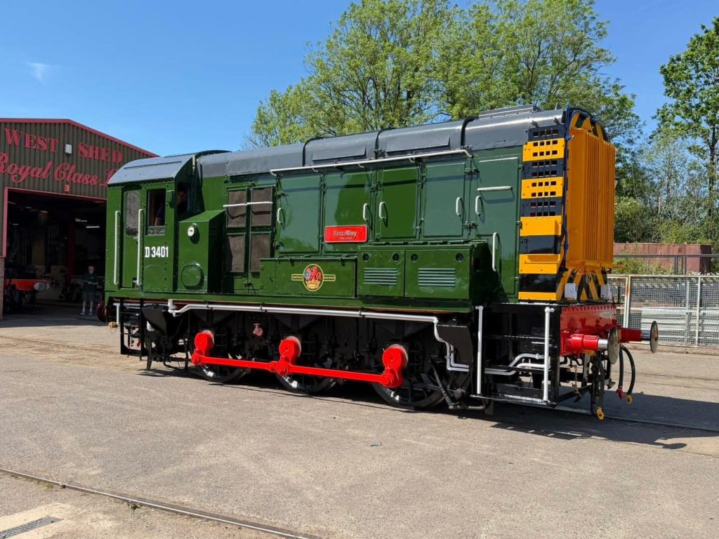 attAg4oJzmzHo5VWs7dXwiFOlCRTCeRPt-ySv9qCUiezMQ - Midland Railway - Butterley Green diesel locomotive on display with red wheels, parked beside a workshop shed (D3401) under a blue sky